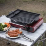 Zwarte grillpan met antiaanbaklaag op een kampeerbrander op een buitentafel met worstjes en groenten
