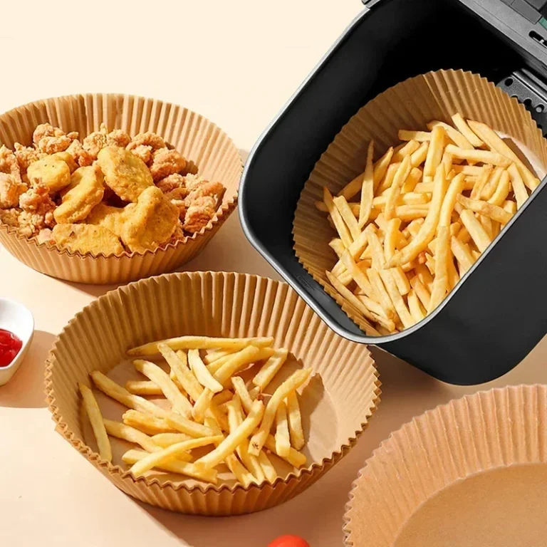 Rond airfryer-bakpapier gevuld met friet en nuggets naast een airfryer